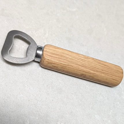 A bottle opener with a silver metal blade and a light brown wooden handle, resting on a light gray textured surface.