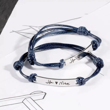 Stack of blue braided bracelets with engraved silver tags on a white surface