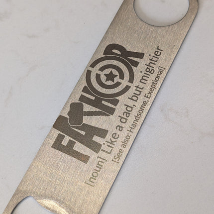 Metallic bottle opener with engraved text on a light gray background
