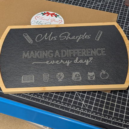 A wooden-framed chalkboard sign with the text 'Mrs Sharples MAKING A DIFFERENCE every day' displayed on a workbench.