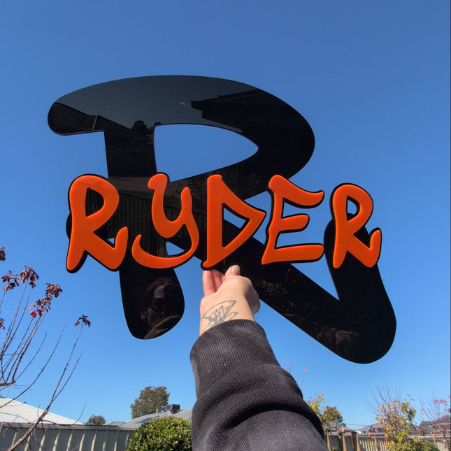 A big black and oragange graffiti wall art in acrylic with the name ryder