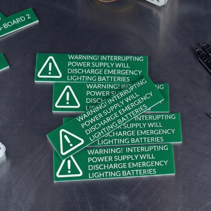 Green warning labels on a dark surface with tools in the background