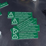 Green warning labels on a dark surface with tools in the background