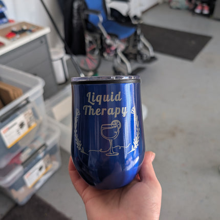 Blue tumbler with 'Liquid Therapy' text held in a hand, garage background