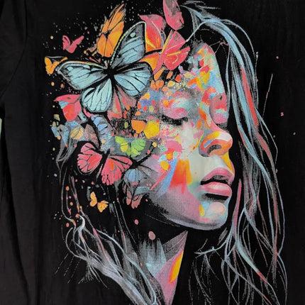 A close-up of a black T-shirt featuring a colorful graphic print of a woman's face with closed eyes, surrounded by vibrant butterflies in pink, orange, yellow, and blue.