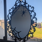 A black Acrylic Halloween mirror with an ornate scrollwork frame and spiderweb design, leaning against a window sill with an outdoor backyard visible in the background.