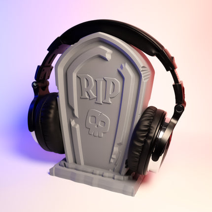 A pair of headphones resting on a gray tombstone-shaped headphone holder with the inscription 'RIP' on the front.