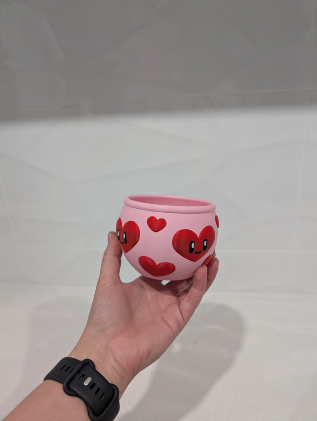 Pink bowl with red heart designs held by a hand on a white background