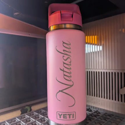 Pink YETI water bottle with 'Natasha' engraved on it, placed on a metal surface.