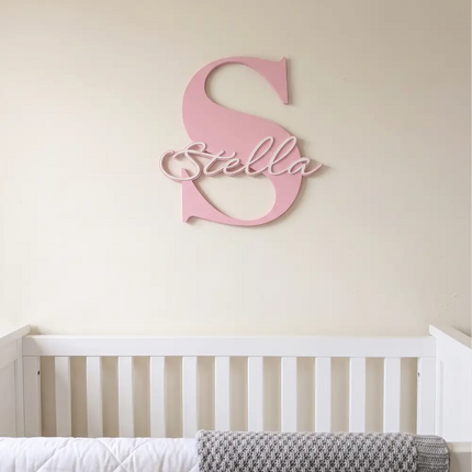 Pink decorative letter 'S' with 'Stella' on a wall above a white crib.