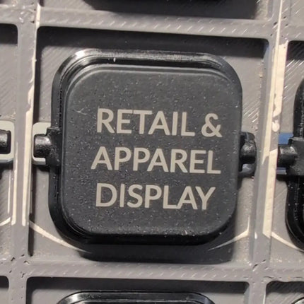 a close up shot of an anthracite clipsal iconic dolly rocker engraved with the words retail and apparel display