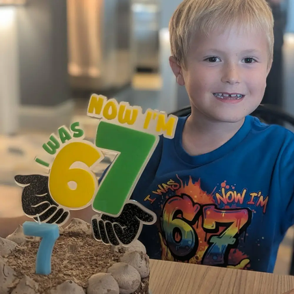 Child wearing a shirt with 'I was 6 now i'm 7' and a birthday cake with a similar design, indoors.