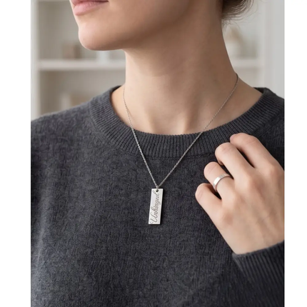 Person wearing a silver necklace with a rectangular pendant, holding it with their hand.